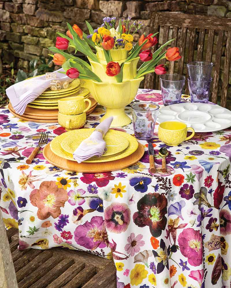 A tablescape with a floral tablecloth and yellow cabbage dishware.
