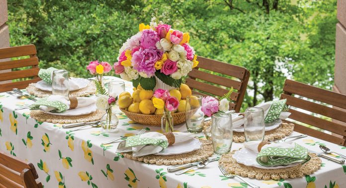 An alfresco tablescape with a lemon printed tablecloth and a floral centerpiece surrounded by lemons.
