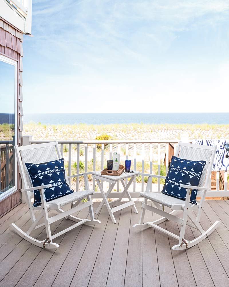 A pair of white rocking chairs on a balcony overlooking the ocean.