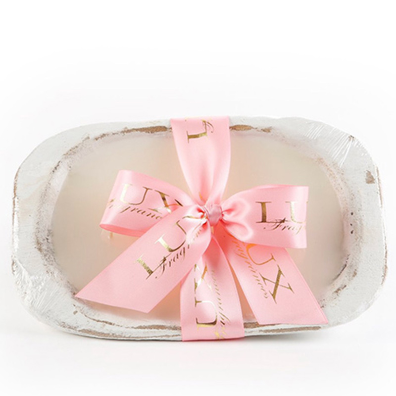 A white dough bowl candle with a pink ribbon.