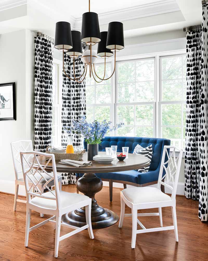 A breakfast nook with a blue velvet bench and black-and-white curtains.