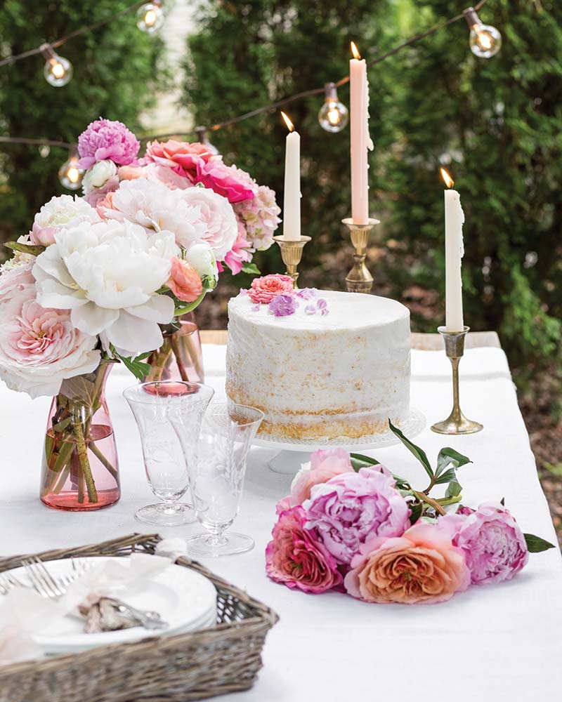 A tablescape with pink flowers, a cake, and candles.