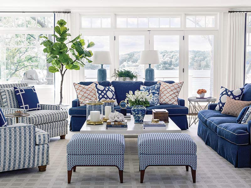 A great room with blue sofas, striped armchairs, and a wall of windows with lake views.