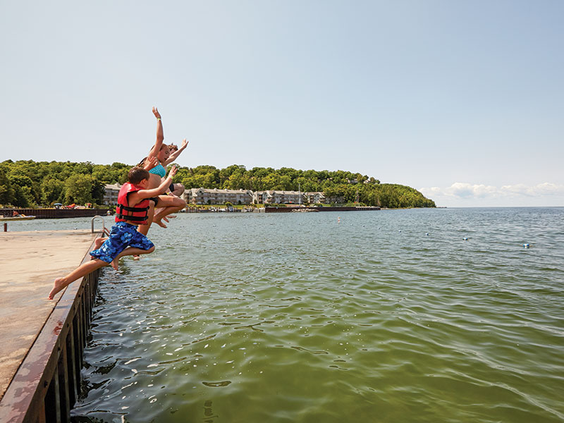 A group of kids jumping off a dock into the lake.