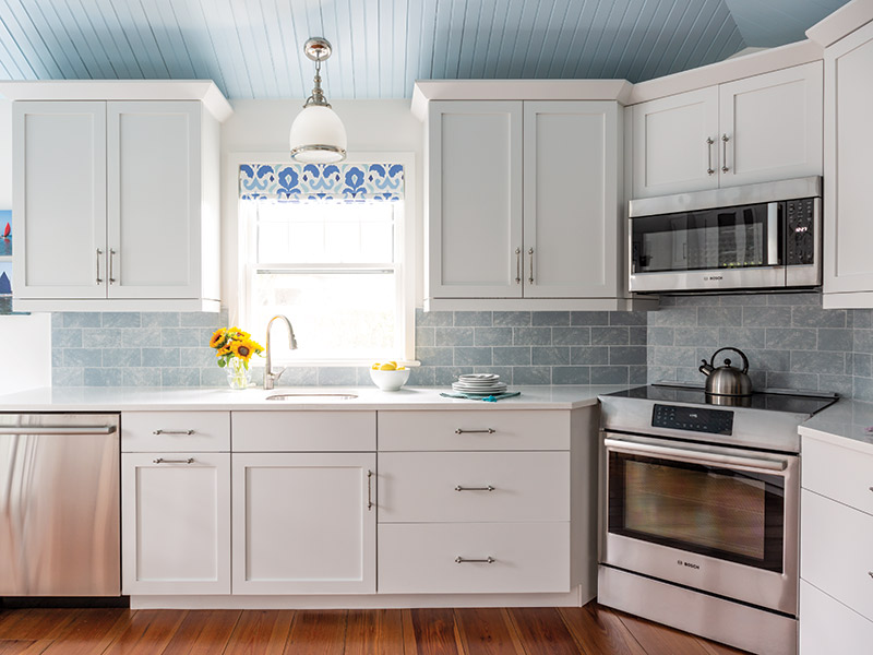 A kitchen with white cabinets and light blue tile backsplash.