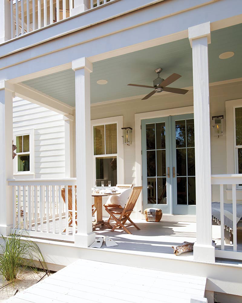 A white porch with a blue ceiling and blue French doors.