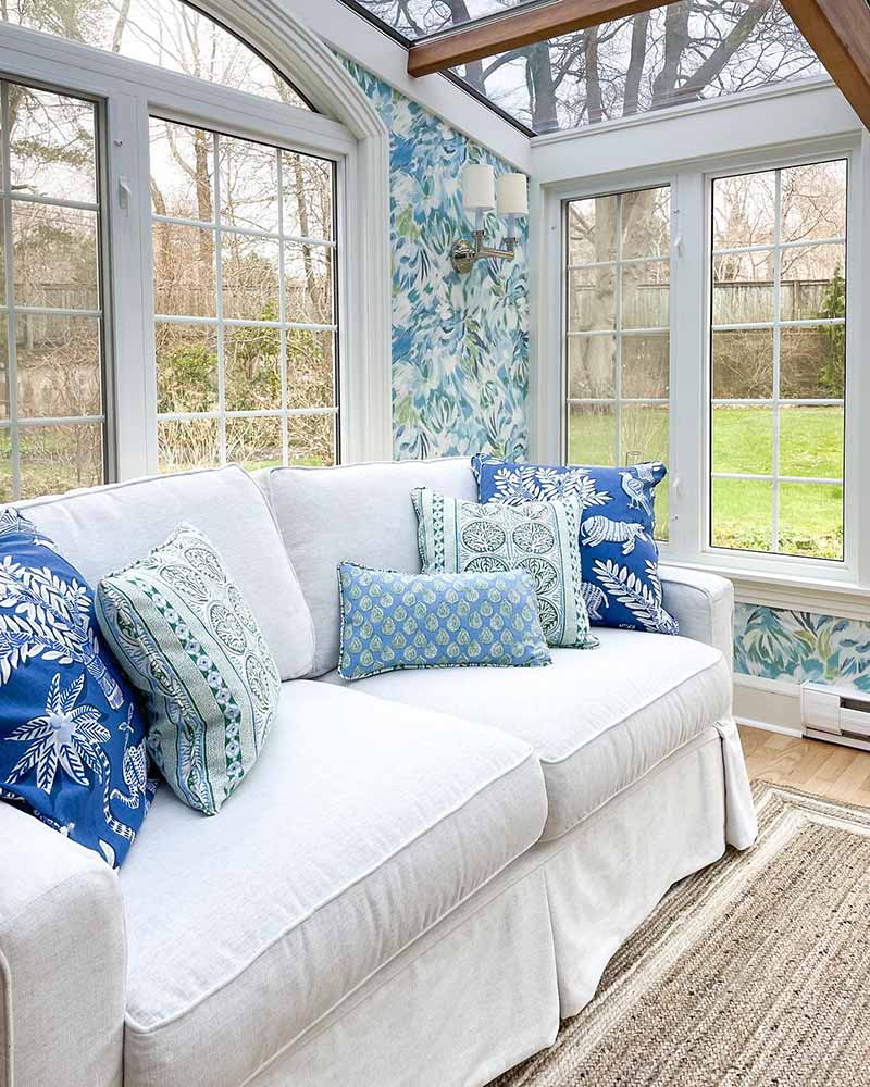 A sunroom with vibrant wallpaper and patterned throw pillows.