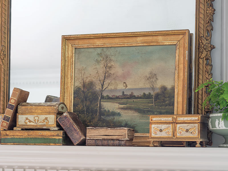 A mantle decorated with antique boxes and artwork.