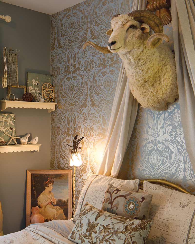 Bedroom with leaning portrait, mounted ram's head over headboard