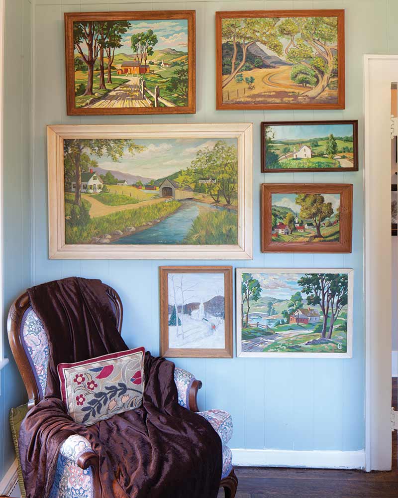 Living room corner, multiple landscape paintings on a wall, arm chair in the corner